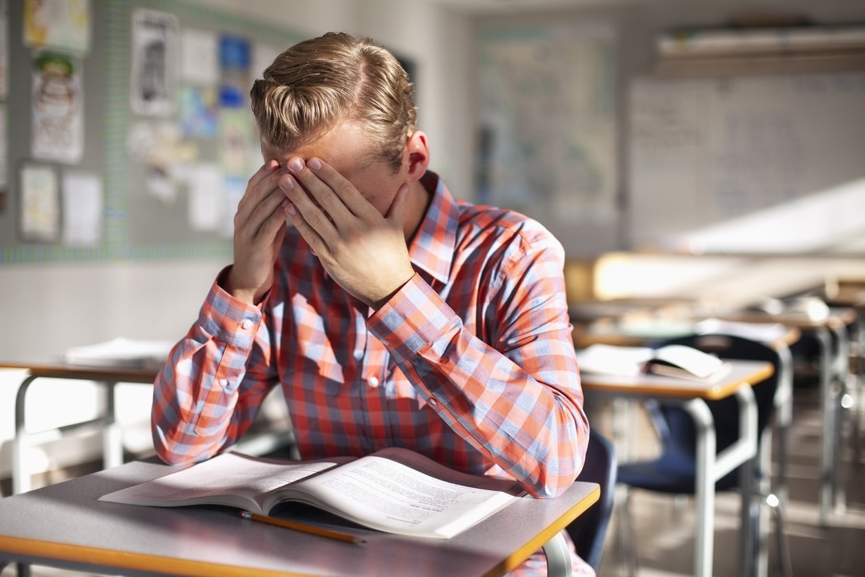 Stressed male student sitting with book at desk